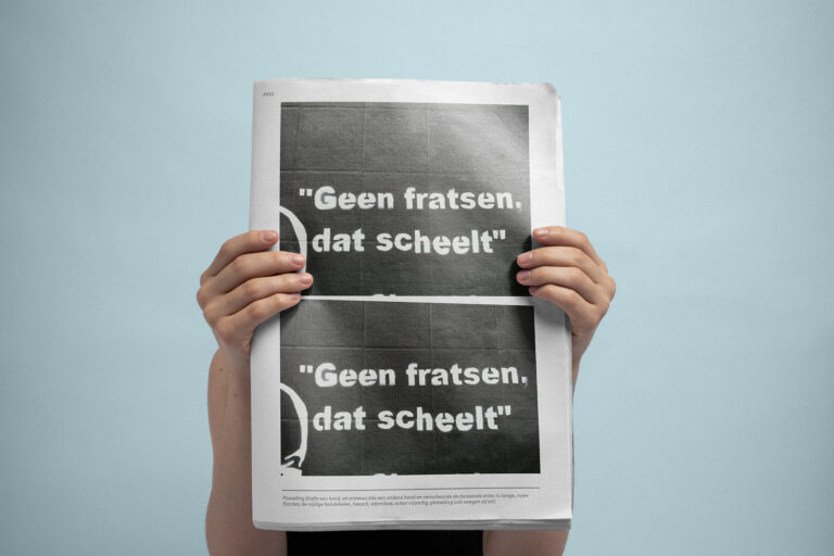 Two hands holding a newspaper in front of the camera with the text 'Geen fratsen dat scheelt'.